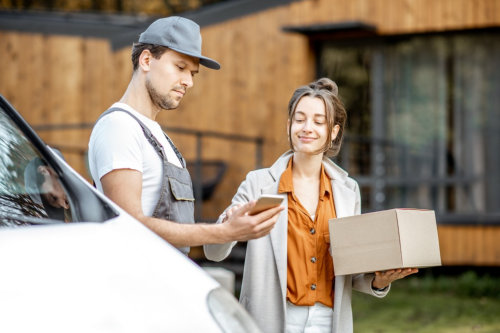 woman signing on a smartphone while receiving parcel near home
