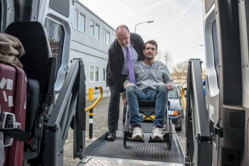 Professional cab driver assisting man on wheelchair to board hydraulic lift van